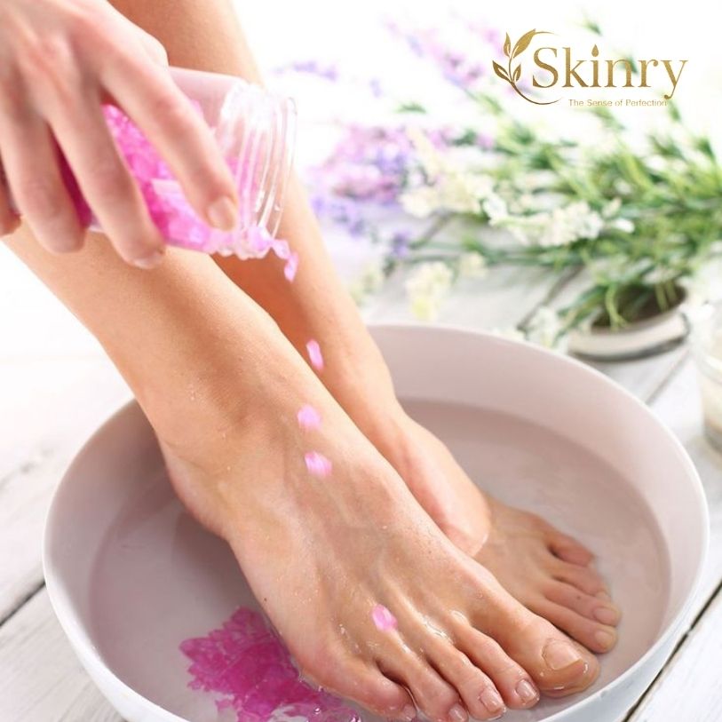 Skinry Store bath salt and foot spa with pink salts poured over feet soaking in a white basin for relaxation