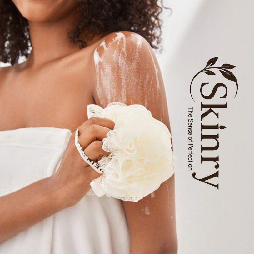 Person using body scrubber loofah to lather and exfoliate shoulder while wrapped in a towel