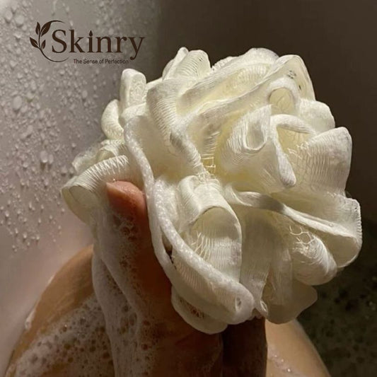 White mesh bath pouf with soap lather held in hand in shower near Skinry logo body scrubber loofah